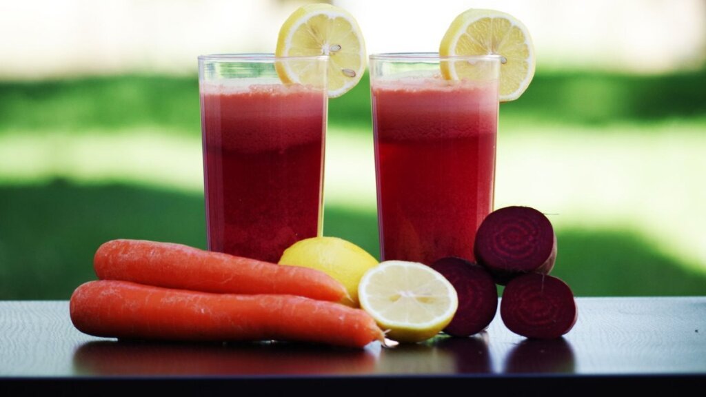 Dos vasos de zumo natural rojo con zanahorias, limon y remolacha